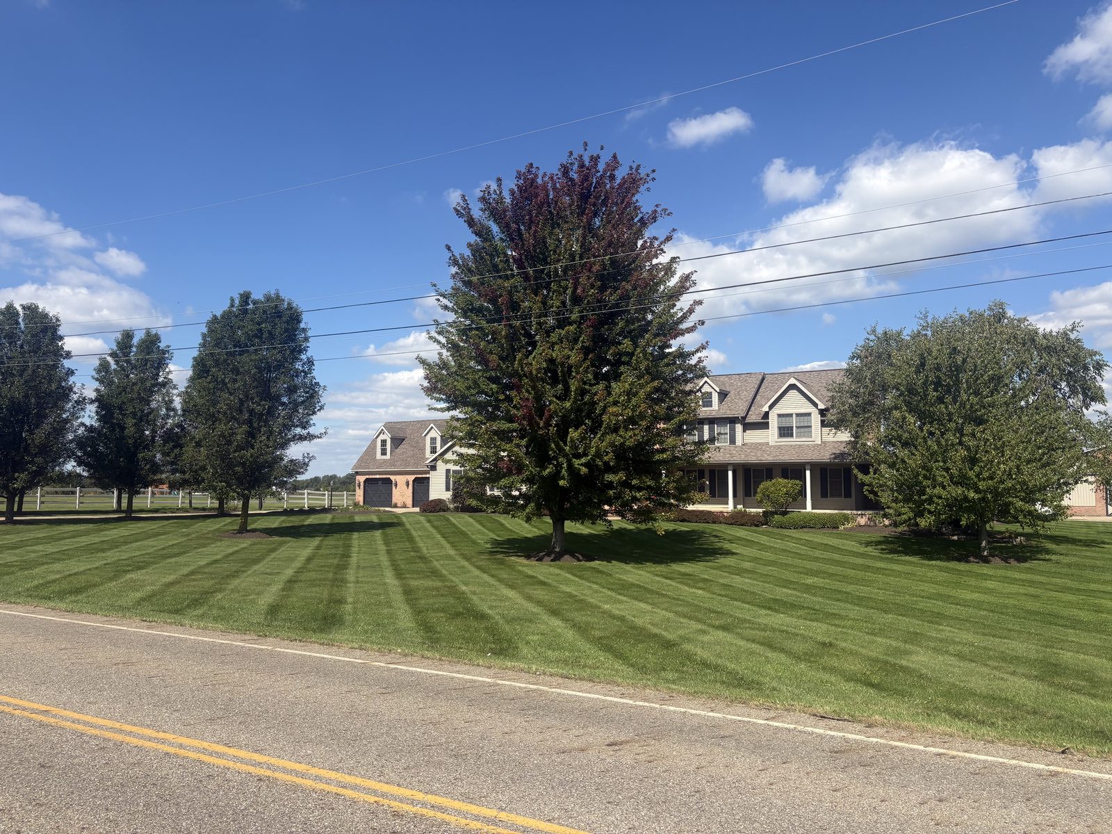 Striped lawn in front of farmhouse with mature trees
